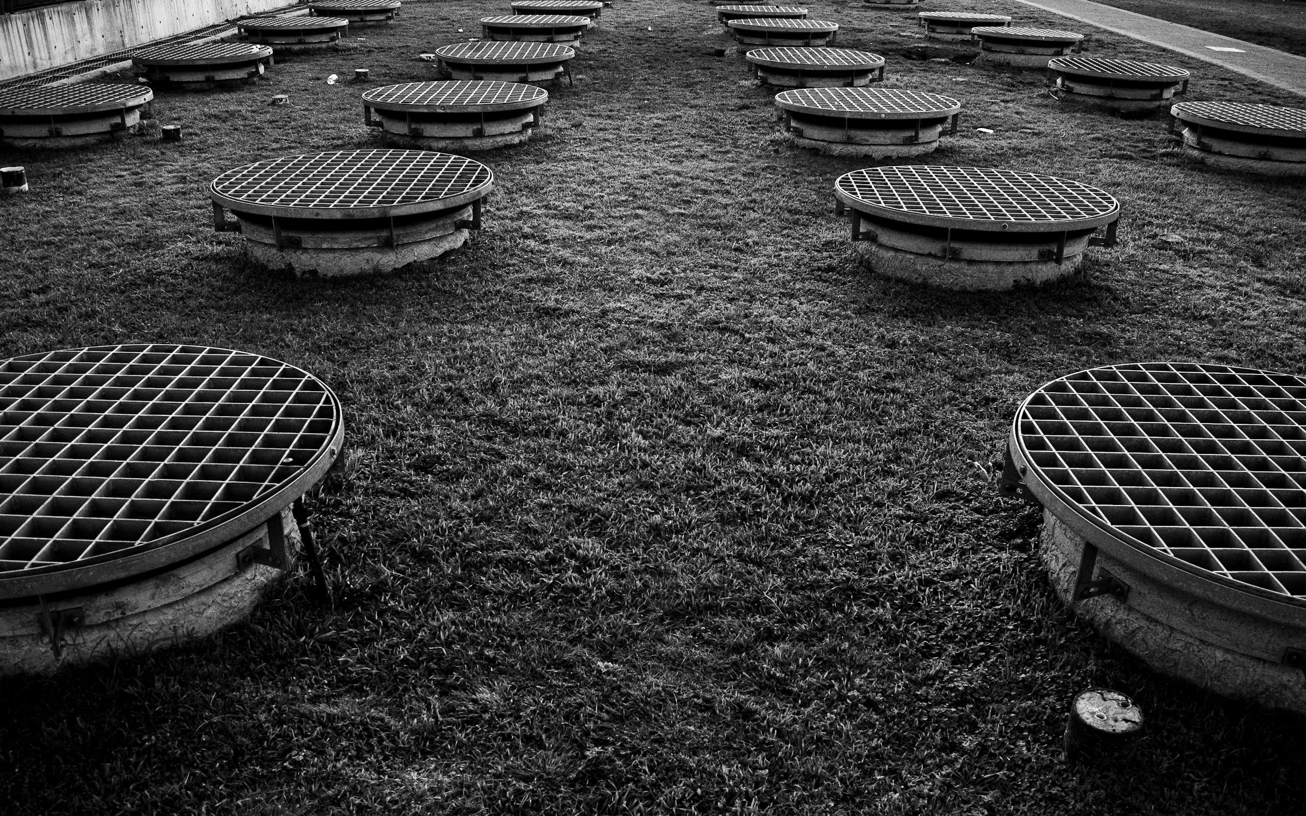 Black and white photo of grid manhole covers on grass in Buenos Aires.